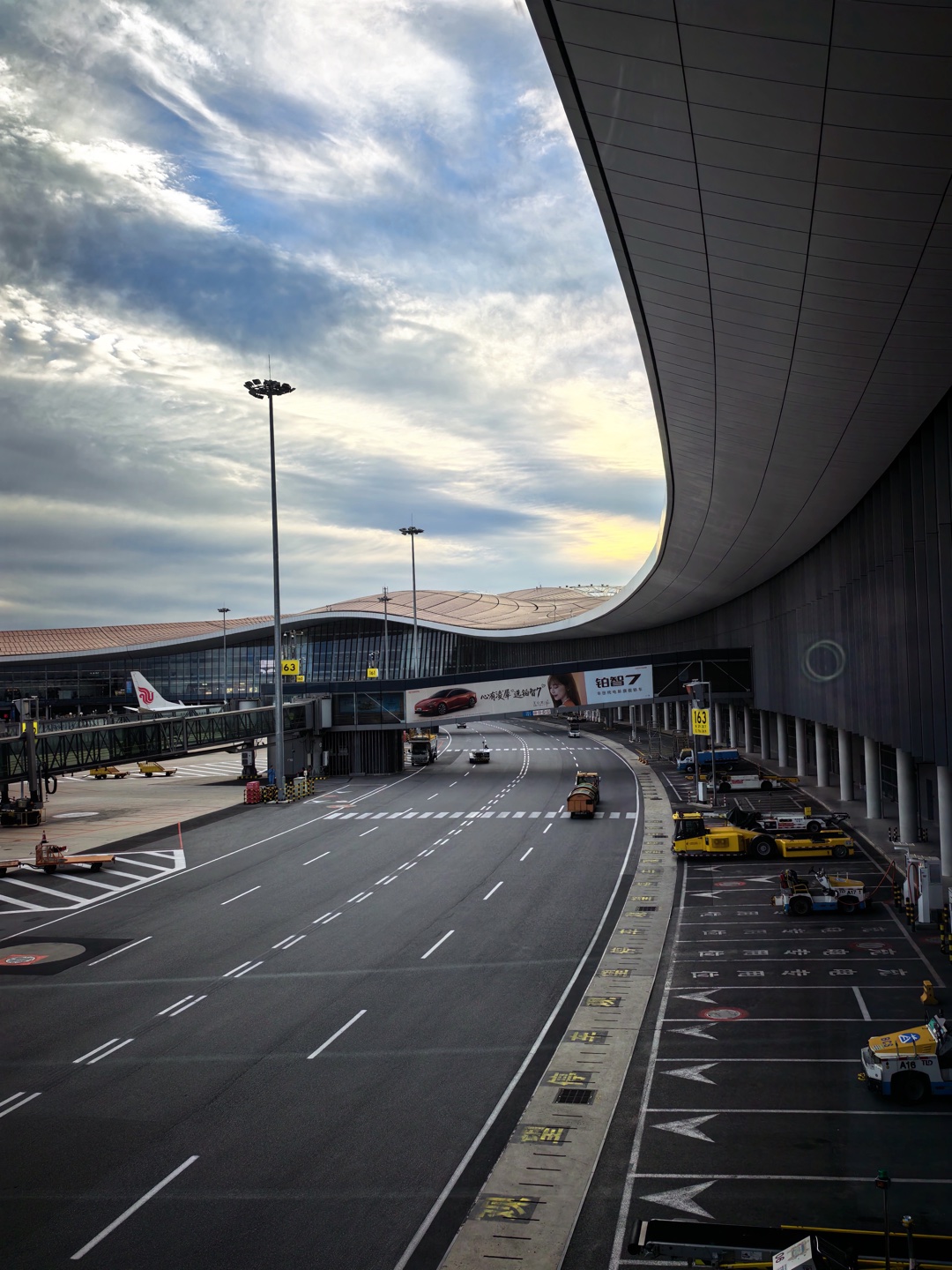 北京大兴机场，弧形航站楼屋顶延伸向云层与夕光下的停机坪。